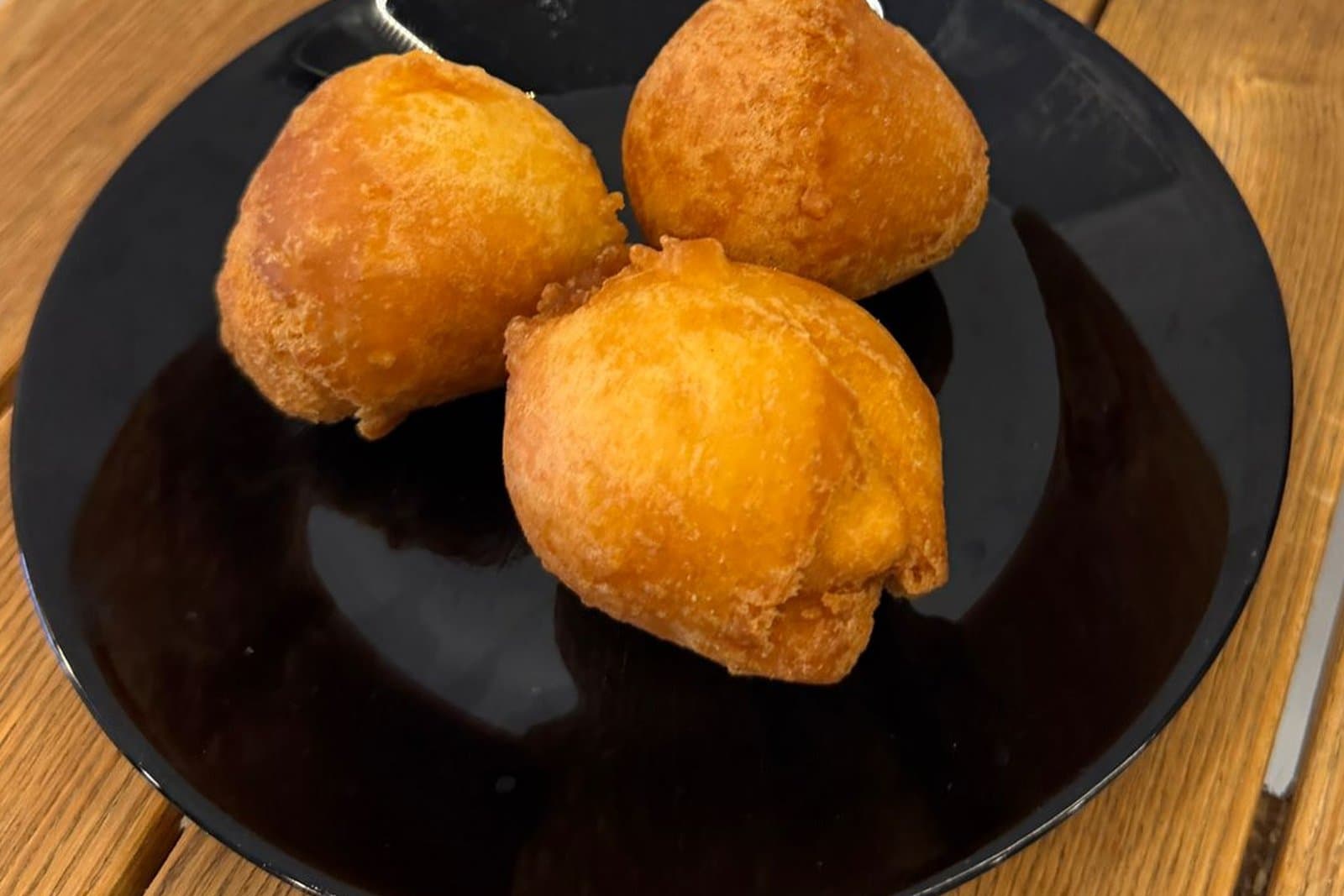 Trois beignets dorés dans une assiette noire