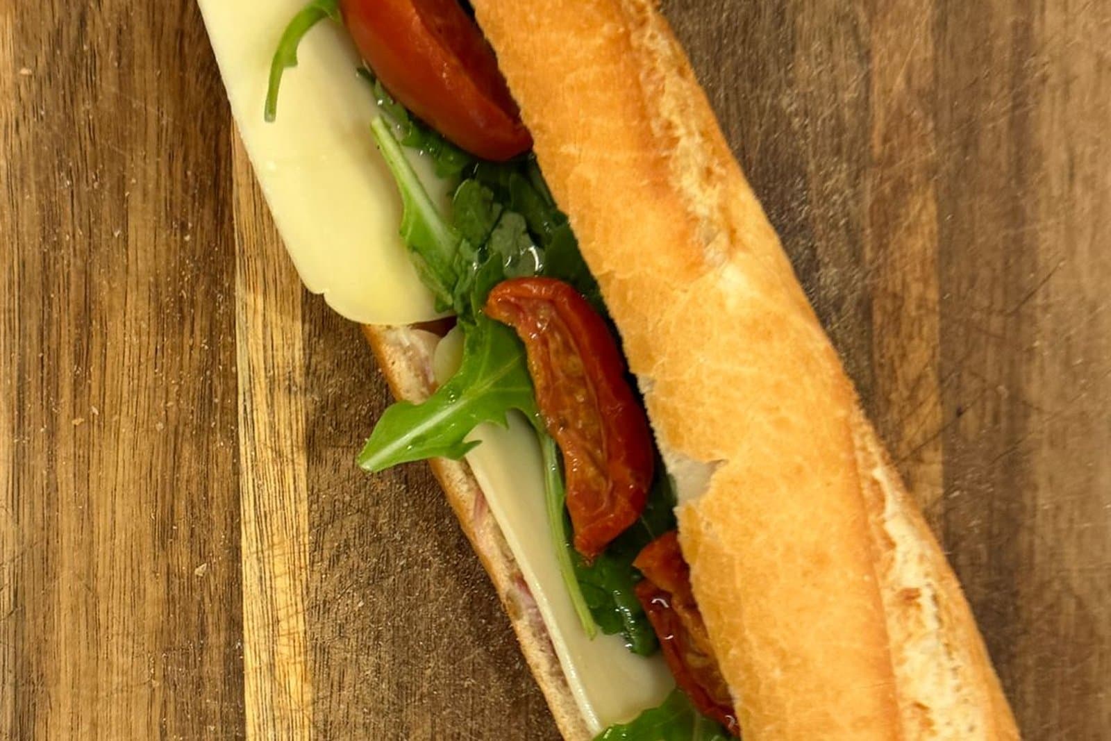 Une baguette italien : jambon, mozzarella, tomates séchées et roquette, sur une planche